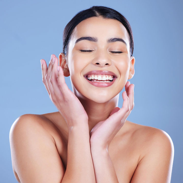 Smiling woman touching her face and showing clear, glowing skin after a skincare routine.